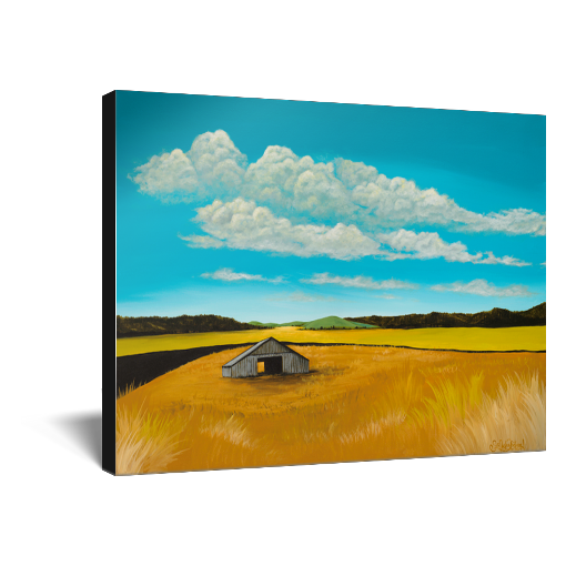 Archival print on canvas of a contemporary rural landscape painting of a rustic barn sitting in a yellow field with green hills in the distance under a blue sky filled with white fluffy clouds. 