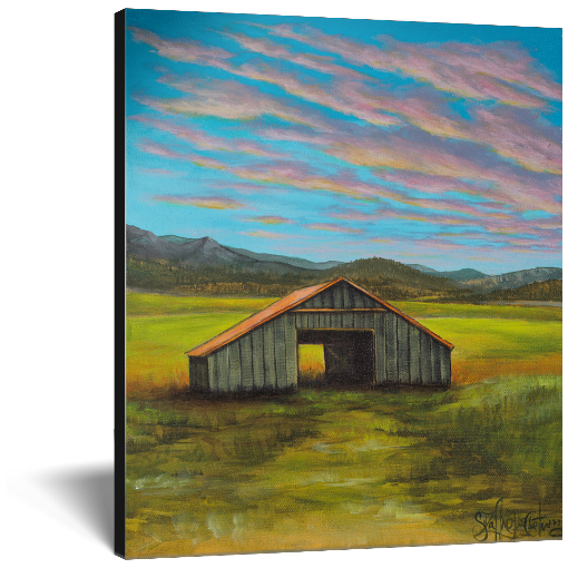Archival print on canvas of a contemporary rural landscape with a rustic barn sitting in a green field with mountains in the distance and a blue sky with pink and yellow sunset clouds. 