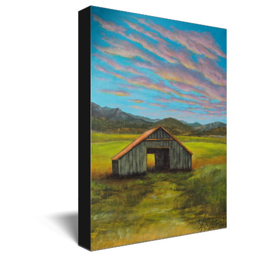 Archival print on canvas of a contemporary rural landscape with a rustic barn sitting in a green field with mountains in the distance and a blue sky with pink and yellow sunset clouds. 