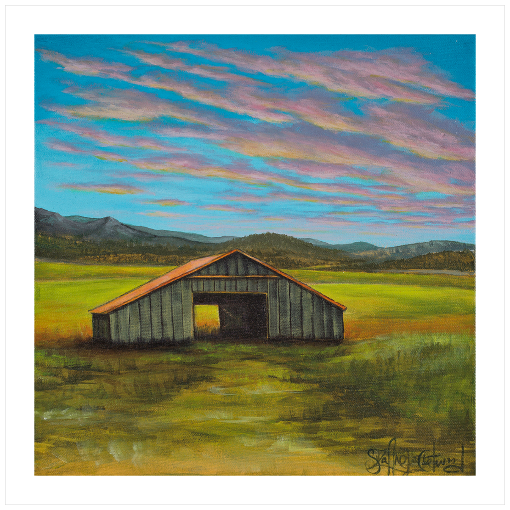 Archival print on matte paper of a contemporary rural landscape with a rustic barn sitting in a green field with mountains in the distance and a blue sky with pink and yellow sunset clouds. 